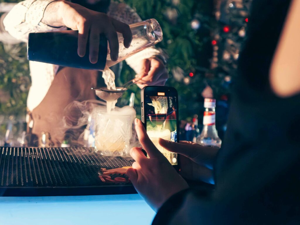 person filming cocktail being poured at bar counter with phone