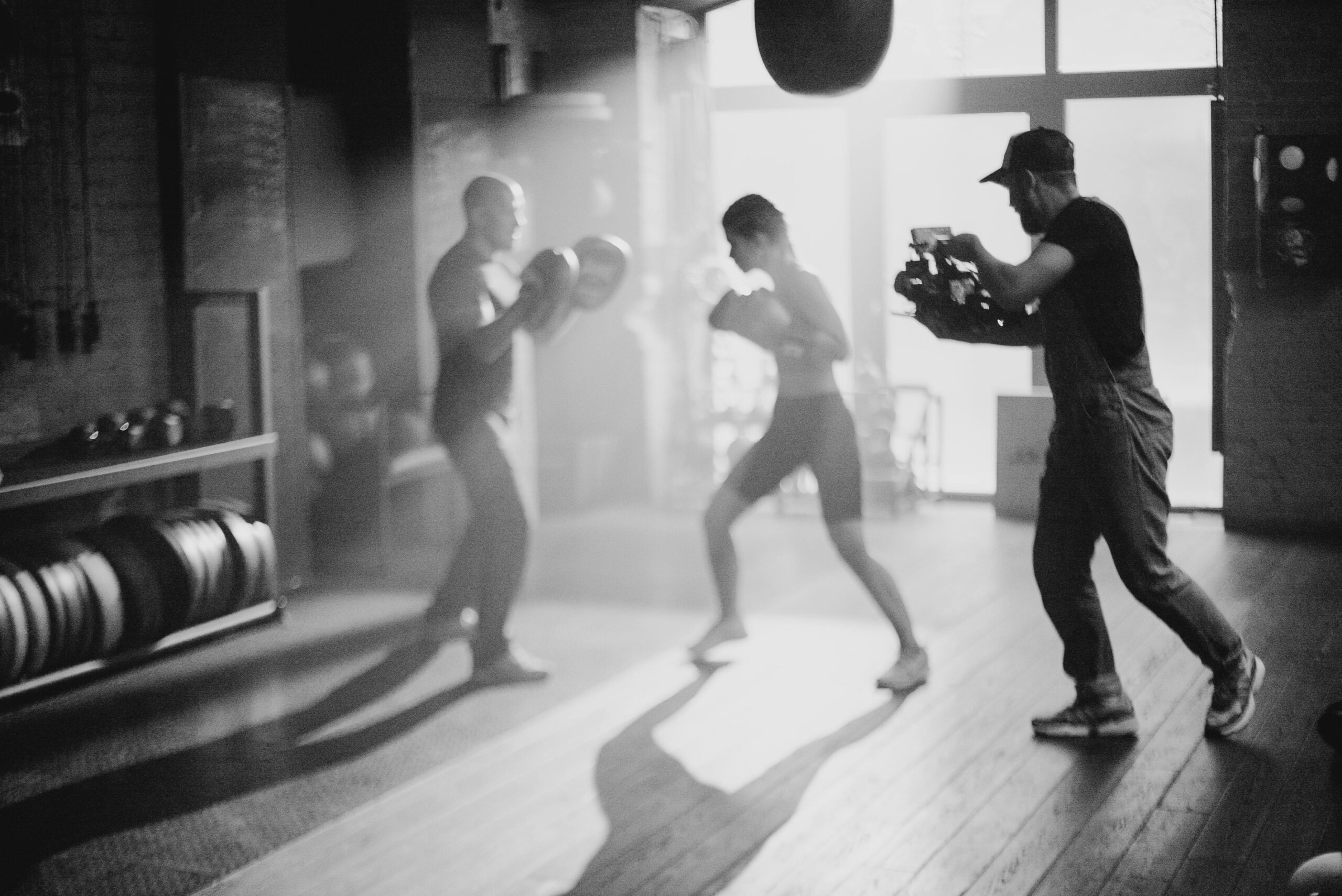 black and white image of videographer filming boxing session in atmospheric gym interior