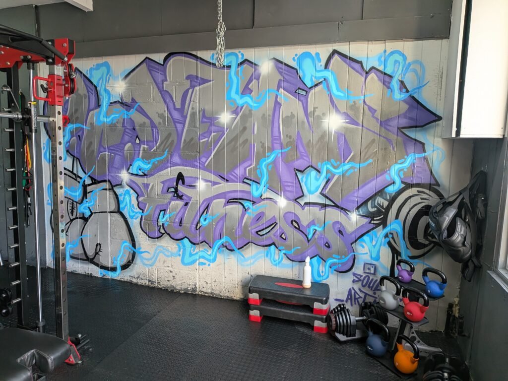 Private gym at O.C. Dean's Fitness Margate with a purple and blue graffiti wall, power rack, kettlebells and dumbbells