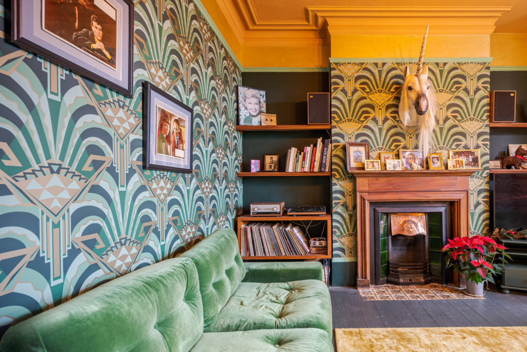 Art deco living room at Margate Delight, green velvet sofa, geometric teal and gold wallpaper, vinyl record collection and a mounted unicorn head