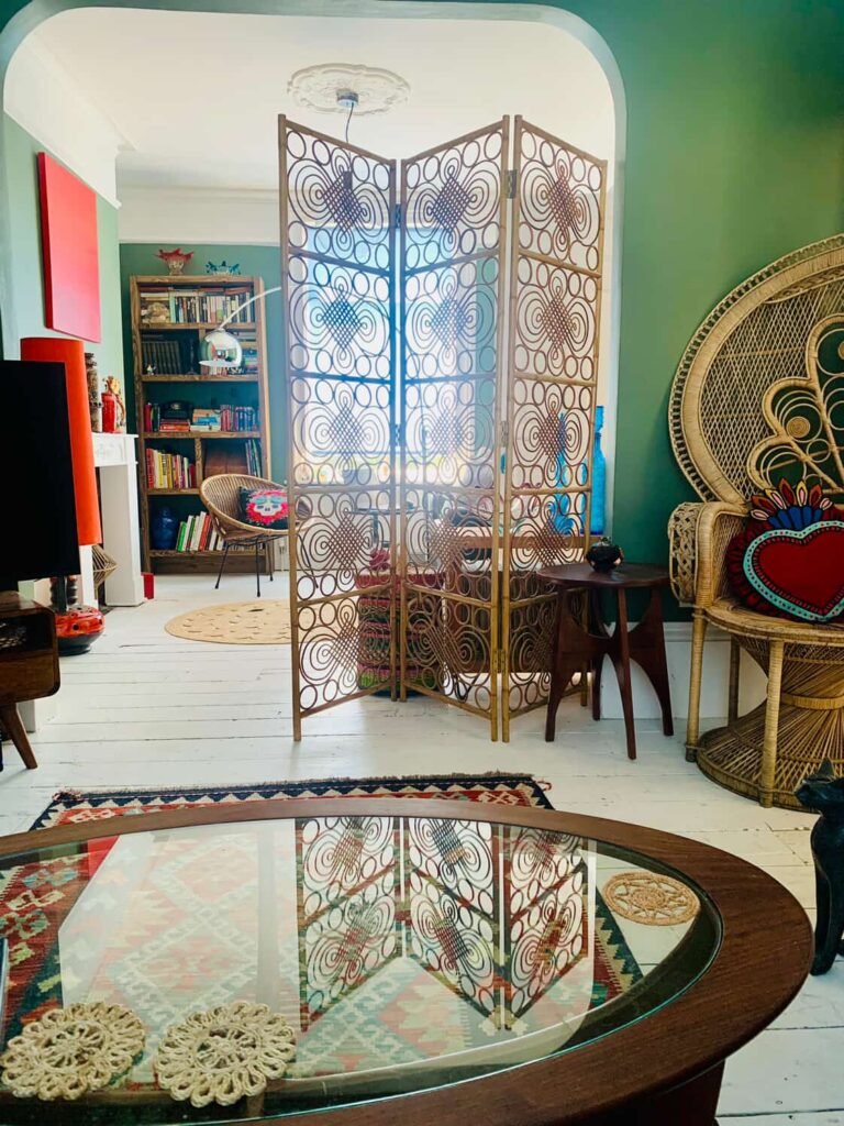 Mid-century sitting room at The Peacock House Margate with rattan peacock chair, cane screen, kilim rug and green walls