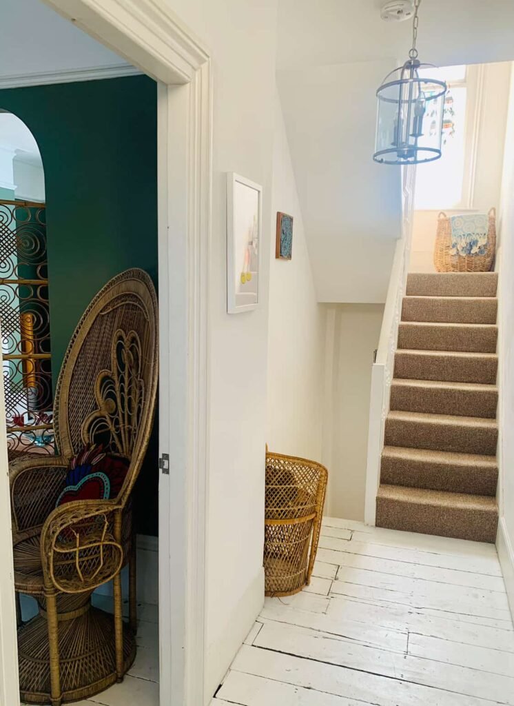 White painted hallway at The Peacock House Margate with staircase and the peacock chair visible through the doorway