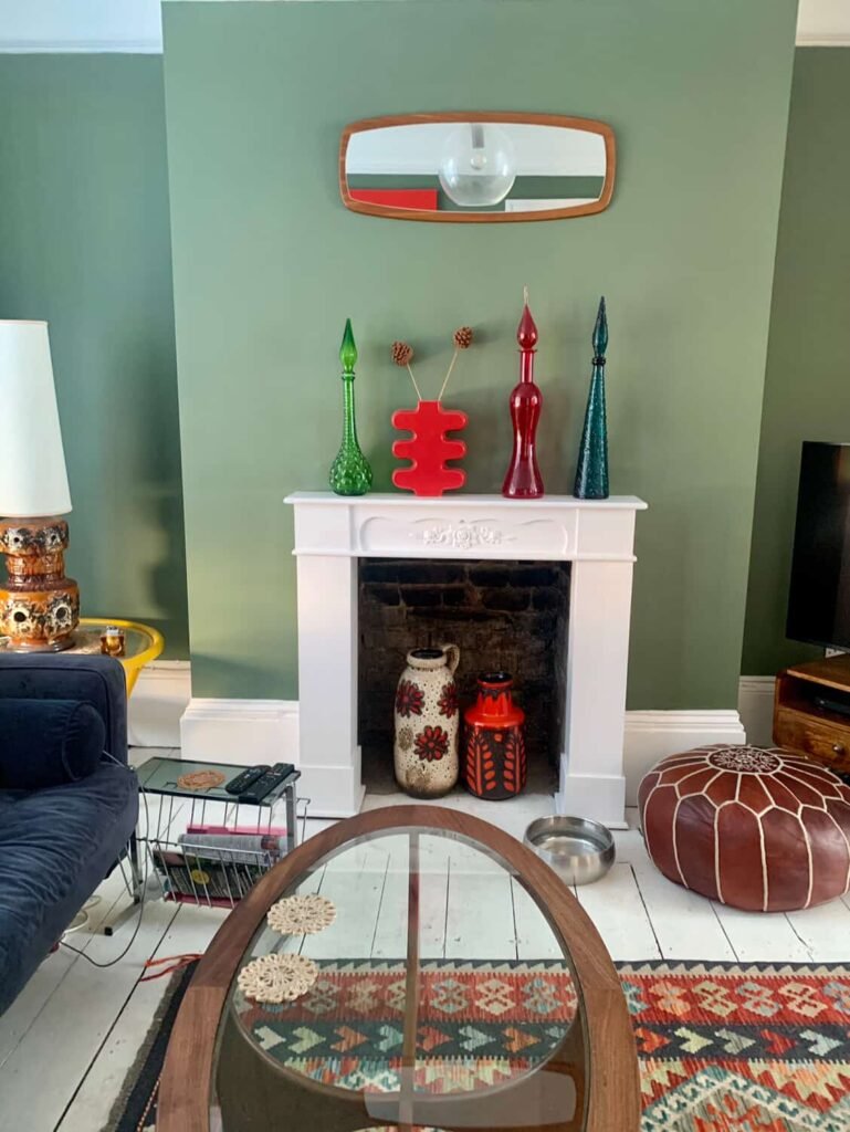 White fireplace at The Peacock House Margate styled with coloured vintage glass decanters against a sage green wall