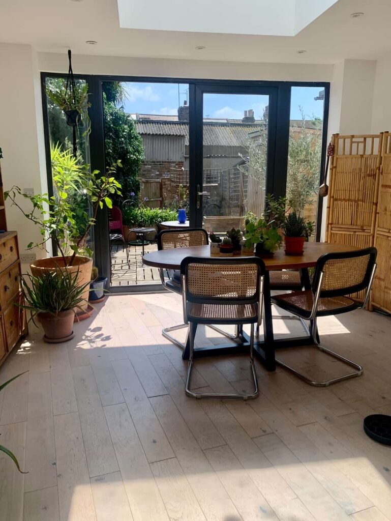Oak dining table and cane chairs at The Peacock House Margate with a bamboo screen and open doors to the decked garden